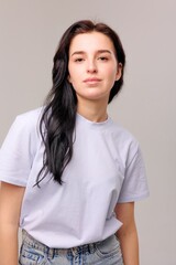 Fototapeta premium Young woman with long dark hair wearing a casual outfit poses confidently against a neutral gray background