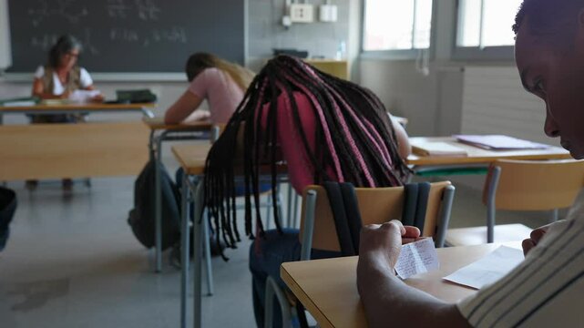 Young teenage boy cheating during examination in classroom at high school. Focus on student hands. Education lifestyle concept.