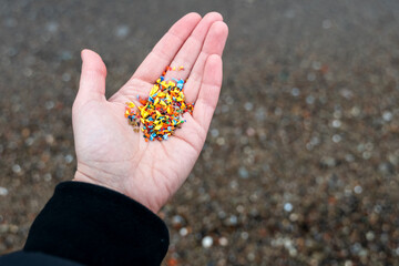 Open palm filled with tiny microplastic particles against blurred sandy sea shore