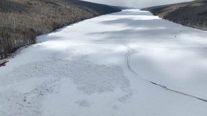Obraz premium Ancient Glacier finger lake Hemlock Lake, NY during Winter in freezing conditions ideal for ice fisherman landscape with cloud shadows on snow covered lake