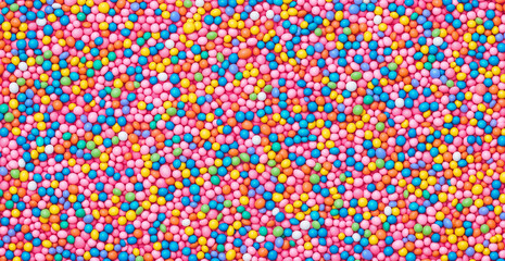 A  of colorful sprinkles on a pink background, viewed from above. The pastel and vibrant colors of the candy sprinkles create a playful and fun atmosphere, with space for text to personalize t