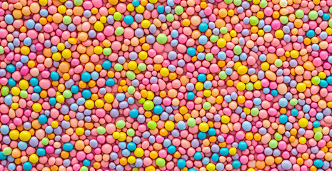Colorful sprinkles pattern on a pink background, creating a seamless texture. The background is a top-down view of colorful candy sprinkles. The colors are pastel and vibrant. Flat lay composition. Sp