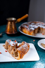 A piece of banana cake or pie and a cup of Turkish coffee on a white plate on a turquoise background. French dessert on the table. Vertical photo.