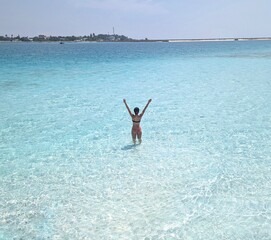 A woman wades through the turquoise, crystal-clear waters of the Maldives, enjoying paradise.