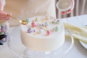 woman making Easter cake in pastel colors in the kitchen, decorating with sprinkles