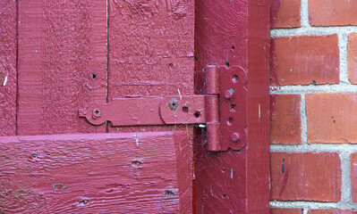 Closeup, red door and hinge with rusty metal for old exterior, damage or vintage doorframe of abandoned home. Empty, entrance or weathered wood with poor lock for bad maintenance or safety breach