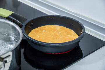 Cooking Omelette in a Nonstick Pan. Close-up of an omelette cooking in a nonstick pan on a modern stovetop, with a pot of boiling water in the background.