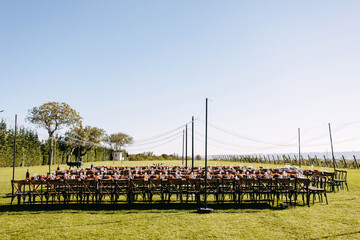 An elegant outdoor wedding reception setup on a lush green lawn with long tables, wooden chairs, and warm floral decorations under string lights