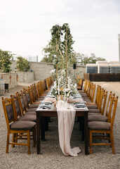 A beautifully decorated outdoor wedding reception long table with wooden chairs, soft blush linens, candles, and greenery.