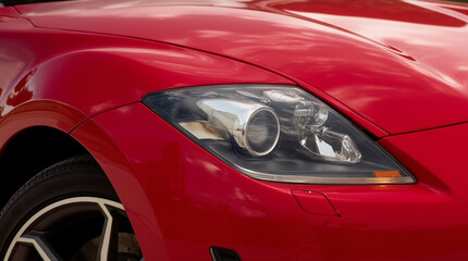 Close-up view of a sleek red sports car showcasing its modern headlight design during golden hour in an outdoor setting