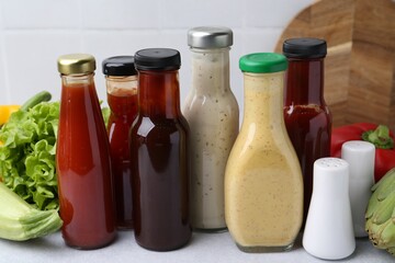 Tasty sauces in glass bottles and fresh products on white table, closeup