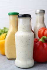 Tasty sauces in glass bottles and fresh products on light grey table, closeup