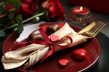 Romantic place setting for Valentine's day. Tableware, cutlery, candies and decorative hearts on grey table, closeup