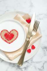 Romantic place setting for Valentine's day. Tableware, cutlery and decorative hearts on white marble table, top view