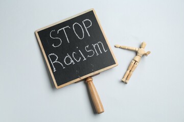 Chalkboard with phrase Stop Racism and human figure on light grey background, top view