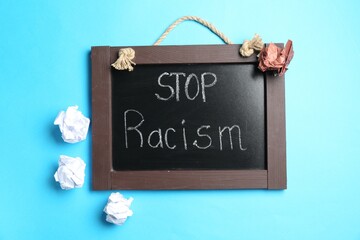 Chalkboard with phrase Stop Racism and crumpled paper pieces of different colors on light blue...
