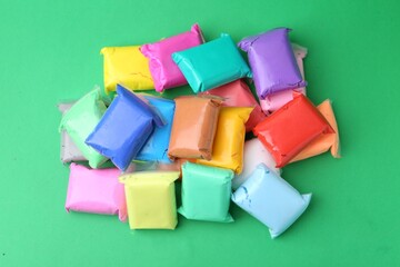 Different colorful play dough in packages on spring green background, top view