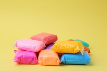Different colorful play dough in packages on yellow background, closeup. Space for text