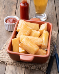 Traditional brazilian fried manioc in a plate with ketchup, pepper and beer over wooden table