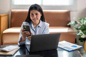 A woman is sitting on a couch with a laptop and a cell phone in front of her