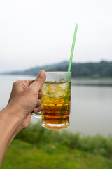 hand holding ice tea with lake background