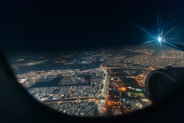 Airplane engine and wing flying over a big illuminated city at night, seen through an aircraft window