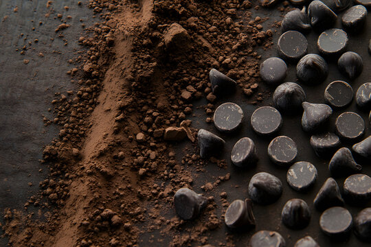 A close-up of chocolate and cocoa powder on the table, with some pieces scattered around. The background is blurred to highlight the details