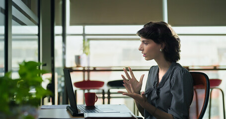 Young adult woman lady sitting use laptop look screen do work online video call client talk new plan indoor office gen z busy expert female girl agent distant help speak share idea job centre place	