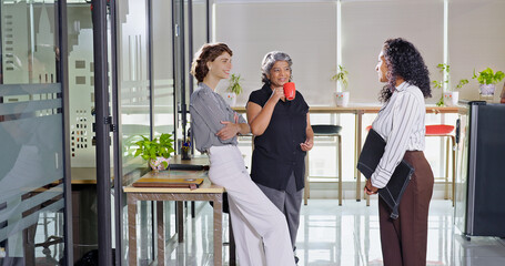 Indian young adult women intern old aged lady hold cup mug drink coffee talk gossip work place...