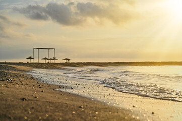 Sunlight glimmers on soft sand as waves break gently along a peaceful beach. Silhouetted umbrellas stand in the distance, capturing the serenity of dusk.