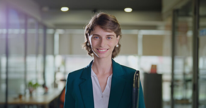 Happy young adult gen z boss ceo woman lady wear blazer formal dress hold carry file folder standing look cam indoor office place proud female expert intern teen girl leader work enjoy job career day
