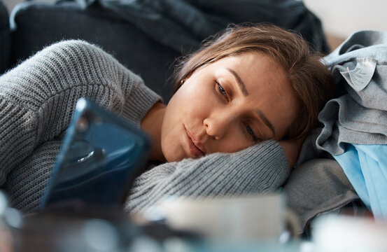 Depressed, lonely or sad woman on sofa with phone for social media addiction or stress in home. Heartbroken, fomo or person reading online story or cyberbullying message on mobile app for bad news