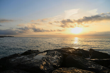 Vibrant hues fill the sky as the sun sets over the tranquil ocean, creating golden reflections on wet rocks along the coastline, inviting serenity and peace.