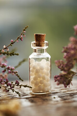 A bottle of white homeopathic pills or globules with pink dried flowers and herbs