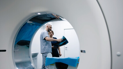 Two doctors in an MRI or CT room reviewing images and discussing the results. The concept of teamwork and precise analysis for diagnosing conditions of organs and the bone system.
