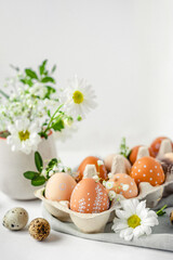 A delicate Easter background with hand-painted eggs in a box on a white table. Easter composition with flowers and feathers