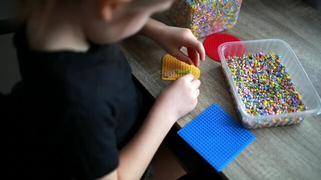  A little girl creates an artistic toy from fusible multi-colored beads. Also known as perler beads. A toy that develops a child's imagination. Close-up of the process.