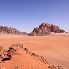 Dramatic desert landscape of Wadi Rum, Jordan, with vast sand plains and towering sandstone mountains. Natural rock formations in warm afternoon light