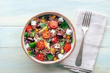 Quinoa salad, healthy Mediterranean lunch with fresh organic vegetables, cheese, and olives, top shot on a wooden background with a spoon