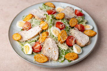 Caesar salad with chicken, cherry tomatoes, croutons, parmesan cheese, quail eggs and romaine lettuce. Traditional American dish. Close-up, selective focus.