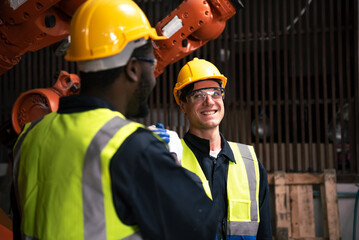 Happy technicians and engineers discussing work and collaborating with teamwork in an industrial factory with a robotic arm.