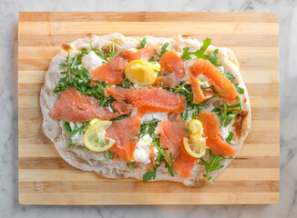 traditional pinsa romana stuffed with salmon, cream cheese and arugula hanging on a
 wooden cutting board