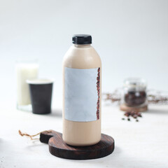 Bottled milk coffee, A creamy drink in an elegant bottle rests on a wooden coaster, accompanied by a coffee cup and glass, showcasing a sophisticated setting