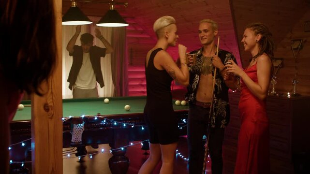 In the foreground a man in black and a woman in red with white shorts kiss holding cups. Behind, a woman in a black dress dances with a man in a floral shirt, while a red friend watches with a drink.