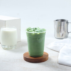 Iced matcha milk, A vibrant green tea drink is placed on a wooden coaster alongside a glass of milk and a metal pitcher, creating a refreshing setup