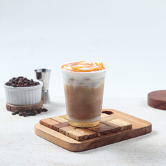 Iced caramel macchiato, Iced coffee drink sits atop a wooden board, adorned with caramel sauce. Coffee beans are arranged nearby, creating an inviting atmosphere