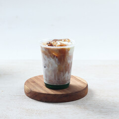 Iced pandan coffee, A refreshing iced coffee drink topped with ice and drizzled syrup sits on a wooden coaster in a simple, clean environment