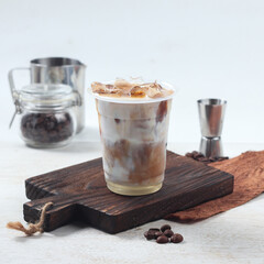 A refreshing iced coffee beverage features cream layered on coffee, placed on a wooden board with coffee beans nearby