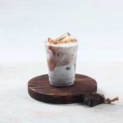 Iced coffee latte, A refreshing iced coffee drink topped with cream and caramel is placed on a rustic wooden coaster against a light backdrop