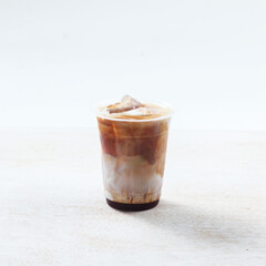 A refreshing iced coffee layered with cream and dark syrup rests on a light surface, perfect for a warm day enjoying a break